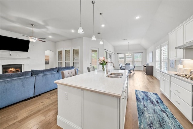 kitchen with sink, white cabinetry, decorative light fixtures, vaulted ceiling, and a center island with sink