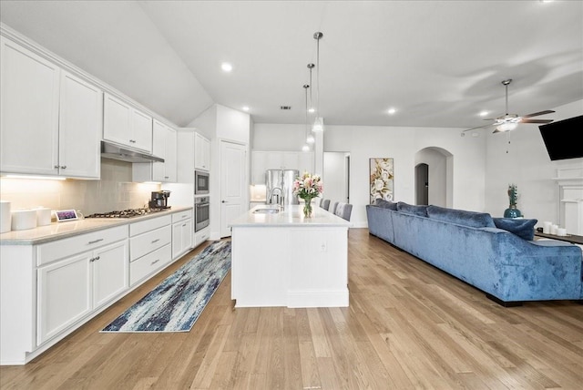 kitchen featuring decorative light fixtures, tasteful backsplash, sink, white cabinets, and a center island with sink