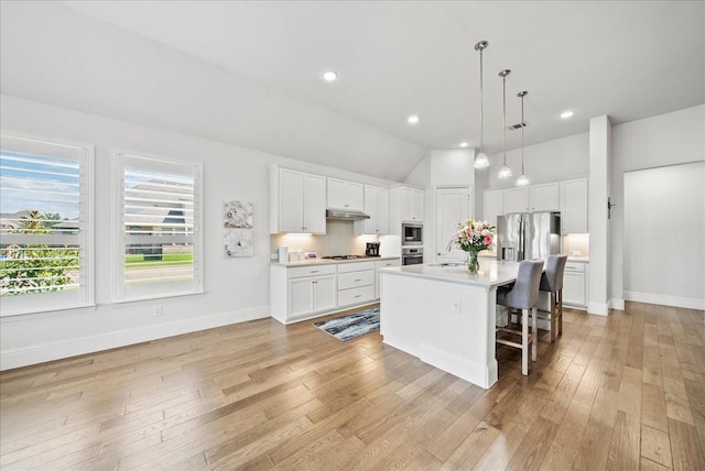 kitchen featuring a breakfast bar area, appliances with stainless steel finishes, hanging light fixtures, white cabinets, and a center island with sink