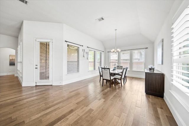 dining space with a chandelier, vaulted ceiling, and light hardwood / wood-style flooring