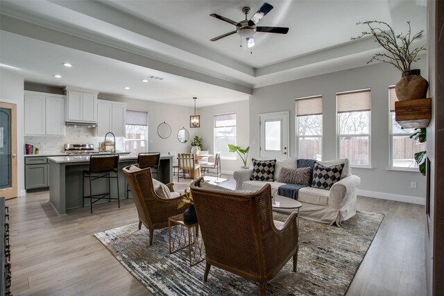 living room featuring sink, light hardwood / wood-style flooring, ceiling fan, and a tray ceiling