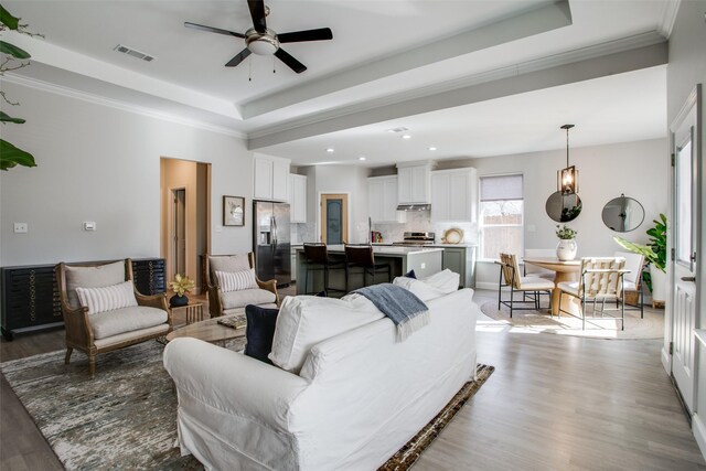 living room with a raised ceiling, ceiling fan, and light hardwood / wood-style flooring