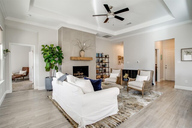 living room featuring a fireplace, a tray ceiling, and light hardwood / wood-style flooring