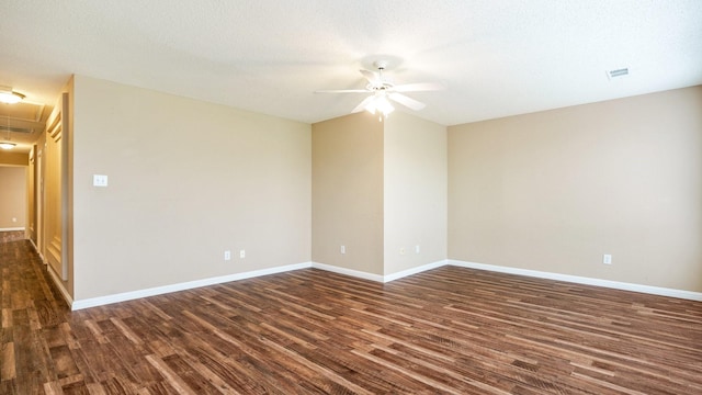 unfurnished room with a ceiling fan, dark wood-style flooring, baseboards, and attic access