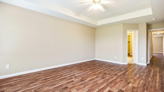 empty room with dark wood finished floors, baseboards, a raised ceiling, and ceiling fan
