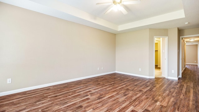 empty room with dark wood-type flooring, a raised ceiling, and ceiling fan