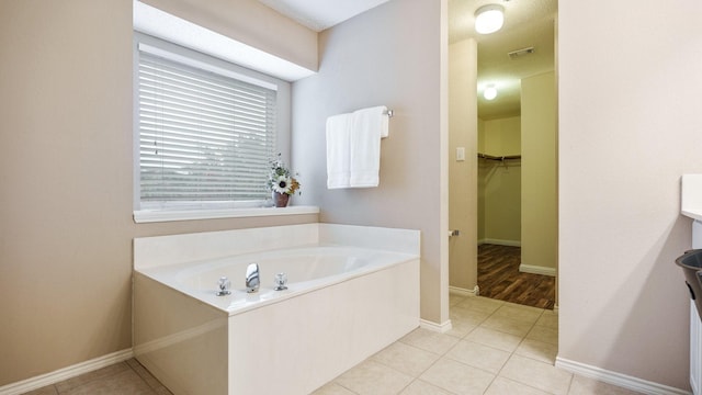 bathroom featuring baseboards, visible vents, tile patterned floors, a walk in closet, and a garden tub