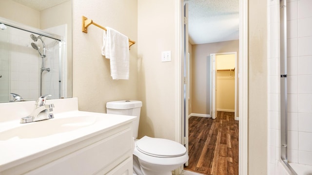 full bath with a tile shower, a walk in closet, toilet, and wood finished floors