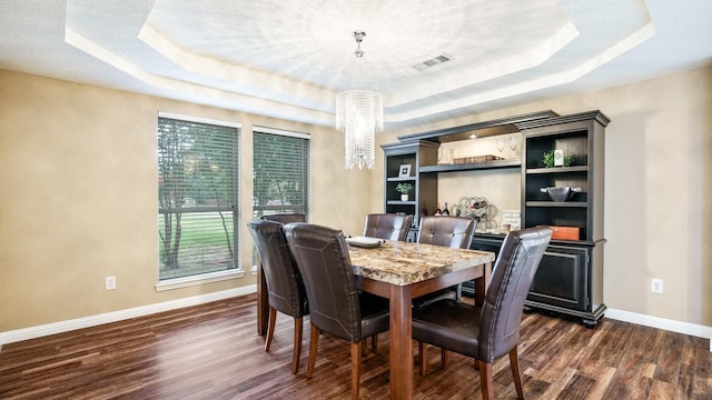 dining area with dark hardwood / wood-style flooring, a raised ceiling, and a chandelier