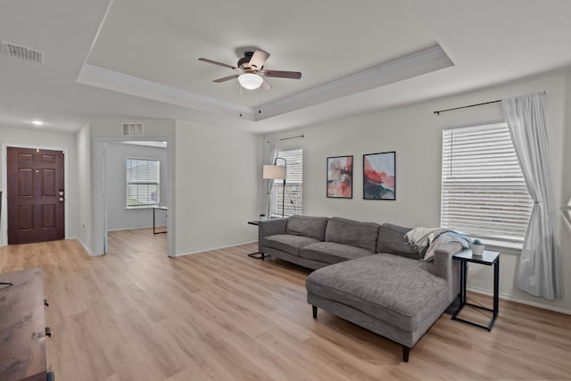 living room with a raised ceiling, crown molding, and light wood-type flooring