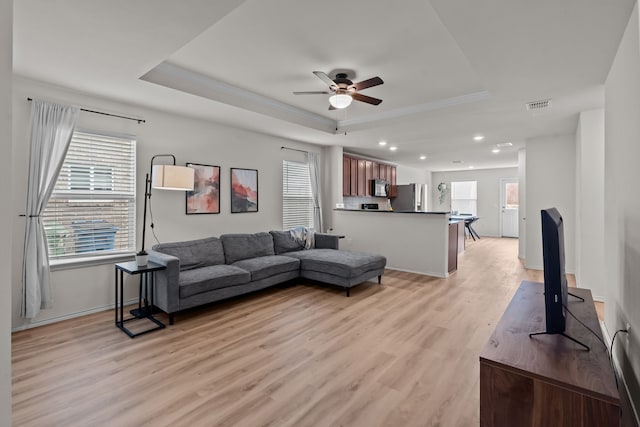 living room with ceiling fan, crown molding, light hardwood / wood-style floors, and a tray ceiling