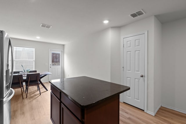 kitchen featuring stainless steel refrigerator with ice dispenser, a kitchen island, dark brown cabinetry, and light hardwood / wood-style flooring