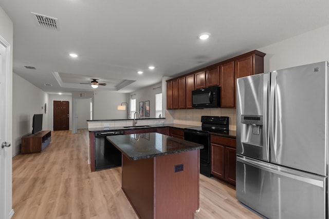 kitchen featuring sink, a raised ceiling, kitchen peninsula, a kitchen island, and black appliances