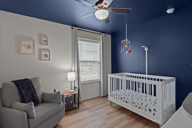 bedroom featuring ceiling fan, hardwood / wood-style floors, and a crib