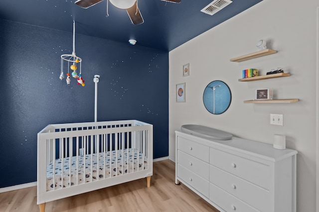 bedroom with a nursery area, ceiling fan, and light wood-type flooring