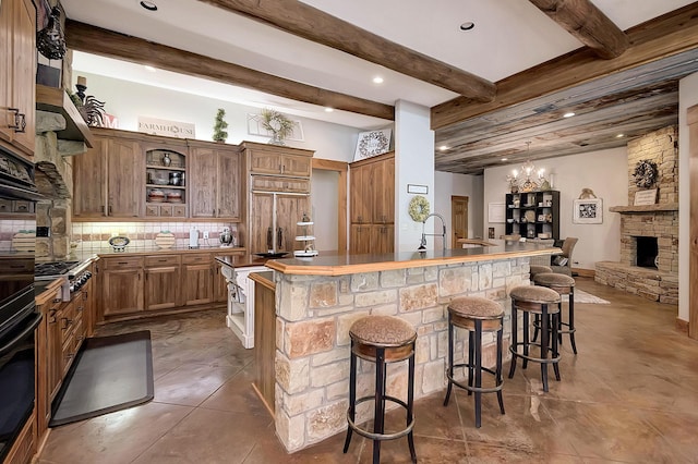 kitchen with a fireplace, a kitchen bar, black oven, paneled fridge, and beam ceiling