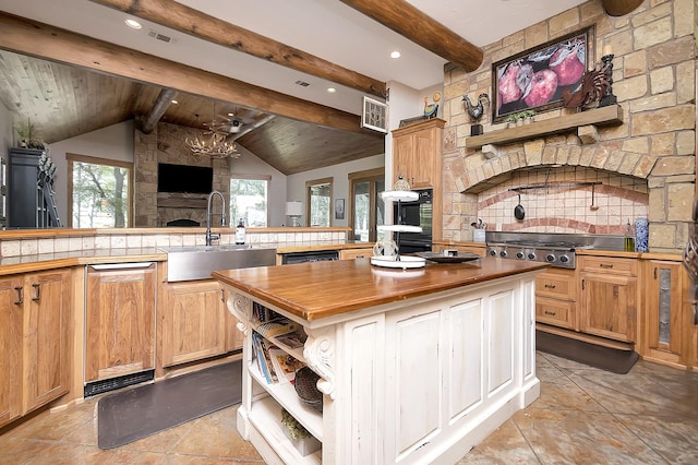 kitchen featuring sink, wooden counters, vaulted ceiling with beams, a fireplace, and a kitchen island