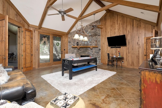 playroom with ceiling fan, high vaulted ceiling, a stone fireplace, beamed ceiling, and wood walls