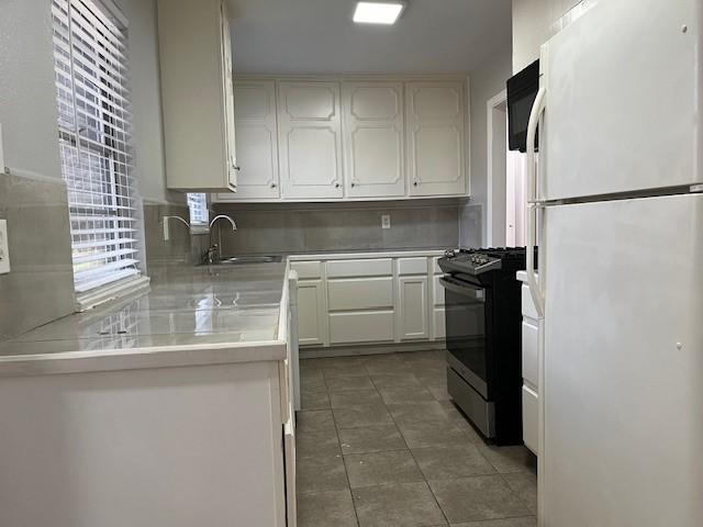 kitchen with white cabinetry, sink, backsplash, white refrigerator, and gas range