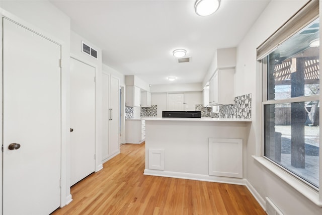 kitchen featuring white cabinetry, decorative backsplash, kitchen peninsula, and light wood-type flooring