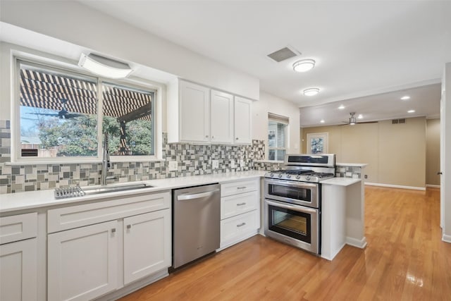 kitchen with white cabinetry, decorative backsplash, kitchen peninsula, stainless steel appliances, and light wood-type flooring