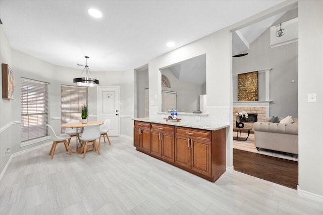 kitchen with decorative light fixtures, a fireplace, light stone countertops, brown cabinets, and lofted ceiling