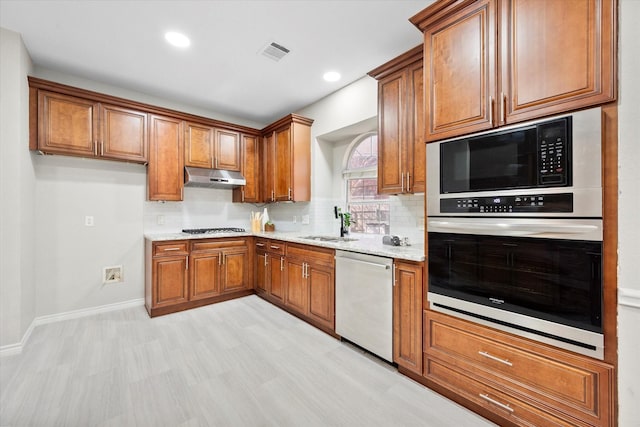 kitchen featuring sink, backsplash, stainless steel appliances, light stone countertops, and light wood-type flooring