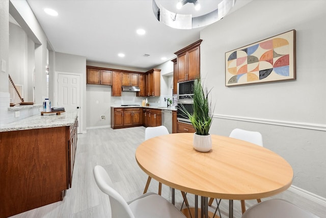 kitchen with brown cabinetry, baseboards, light countertops, under cabinet range hood, and appliances with stainless steel finishes