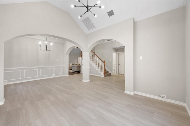 spare room with an inviting chandelier, high vaulted ceiling, and light wood-type flooring