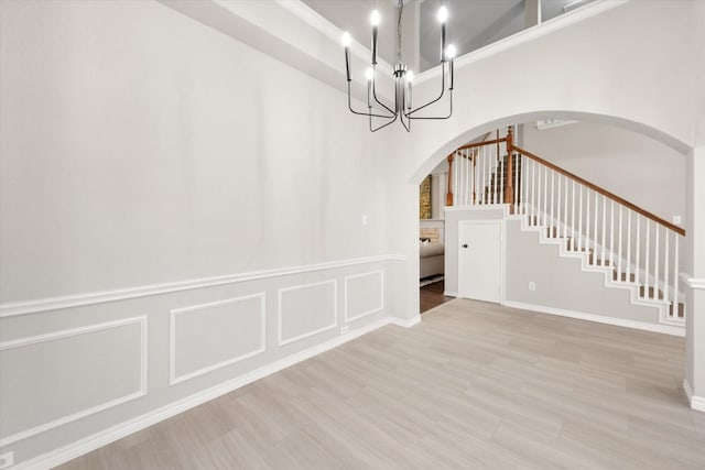 interior space featuring arched walkways, wood finished floors, a chandelier, a decorative wall, and stairs