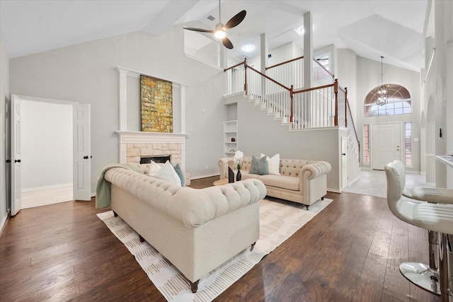 living room with hardwood / wood-style floors, a stone fireplace, ceiling fan with notable chandelier, and high vaulted ceiling