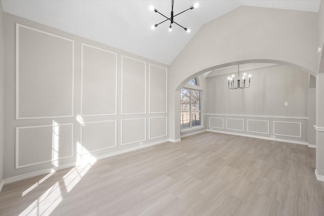 unfurnished living room featuring a decorative wall, high vaulted ceiling, a chandelier, arched walkways, and light wood finished floors