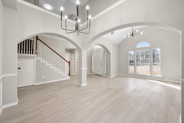 unfurnished living room with an inviting chandelier, stairs, high vaulted ceiling, light wood-type flooring, and arched walkways