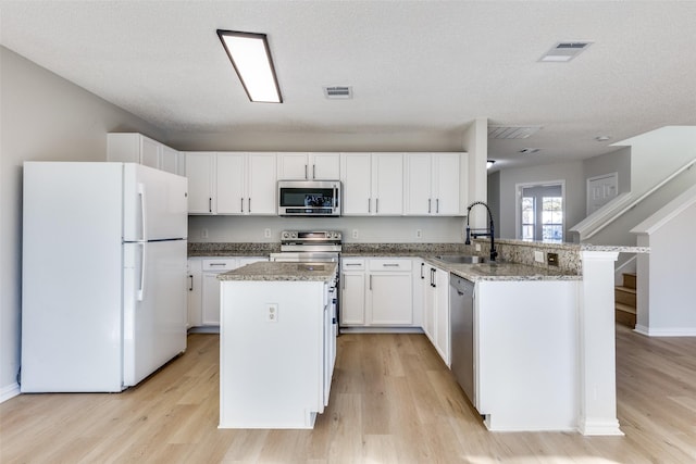 kitchen with sink, appliances with stainless steel finishes, a textured ceiling, white cabinets, and kitchen peninsula