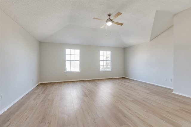 empty room with ceiling fan, vaulted ceiling, light hardwood / wood-style floors, and a textured ceiling