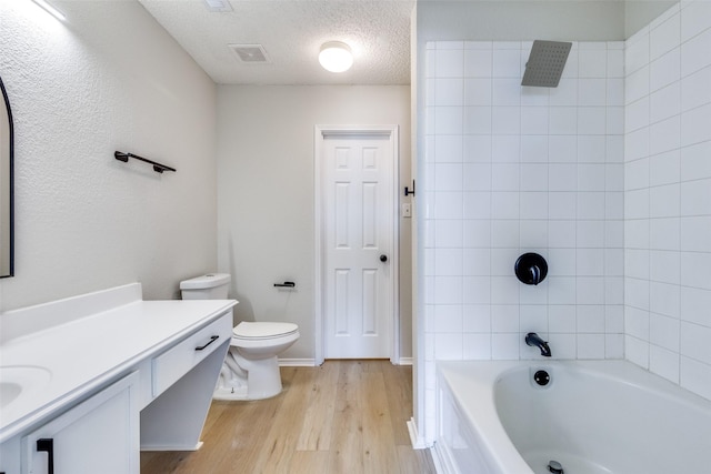 full bathroom with hardwood / wood-style flooring, vanity, tiled shower / bath combo, toilet, and a textured ceiling