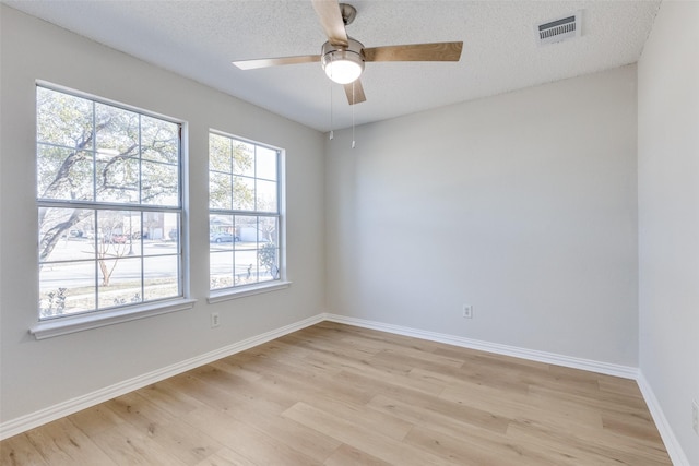 empty room with a textured ceiling, a healthy amount of sunlight, and light wood-type flooring