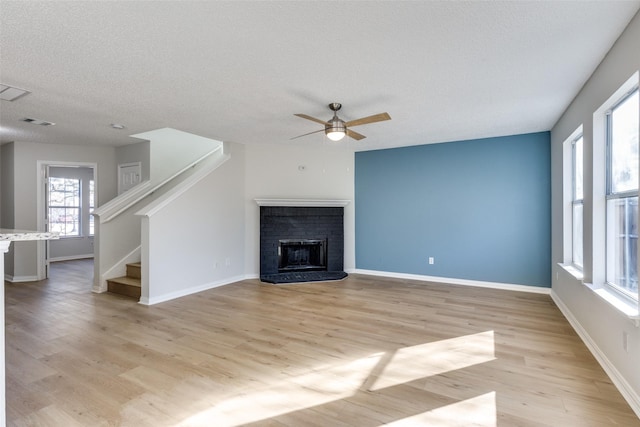 unfurnished living room featuring ceiling fan, a fireplace, light hardwood / wood-style floors, and a textured ceiling