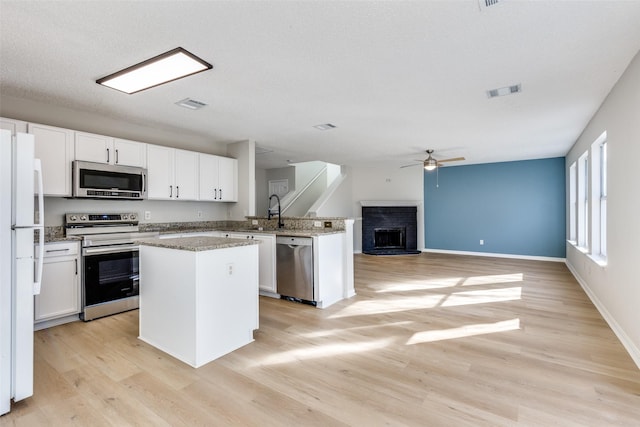 kitchen featuring appliances with stainless steel finishes, white cabinets, a center island, a brick fireplace, and light wood-type flooring