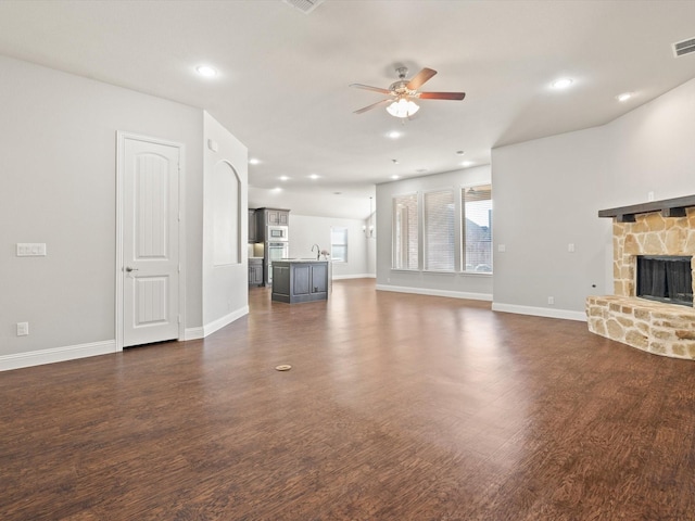 unfurnished living room featuring a fireplace, baseboards, dark wood finished floors, and a ceiling fan