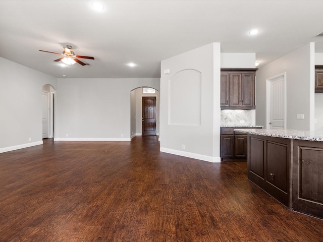 unfurnished living room with arched walkways, dark wood finished floors, baseboards, and ceiling fan