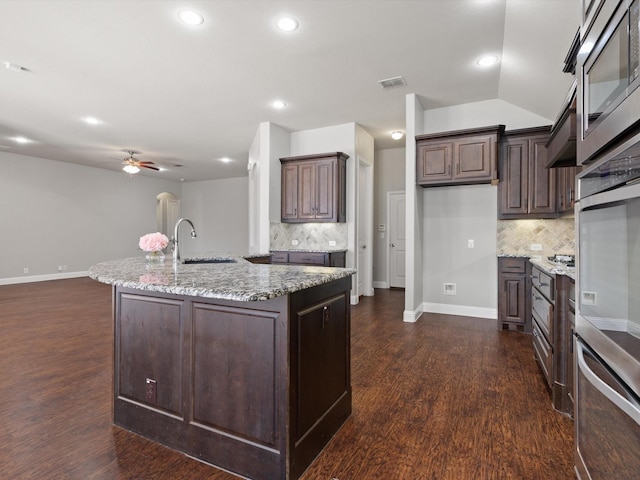 kitchen with light stone counters, dark wood finished floors, visible vents, stainless steel microwave, and a sink