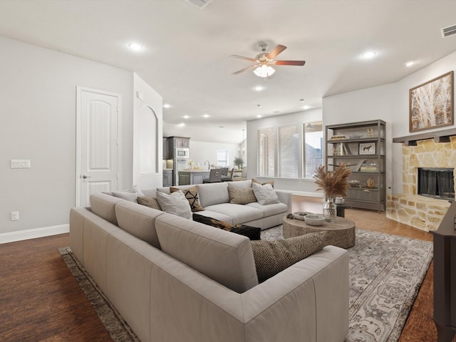 living room featuring a stone fireplace, dark wood-type flooring, and ceiling fan