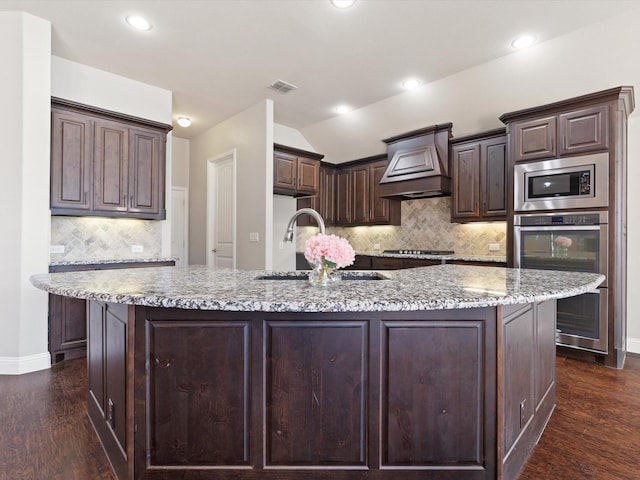 kitchen with visible vents, custom range hood, stainless steel appliances, dark brown cabinets, and a sink