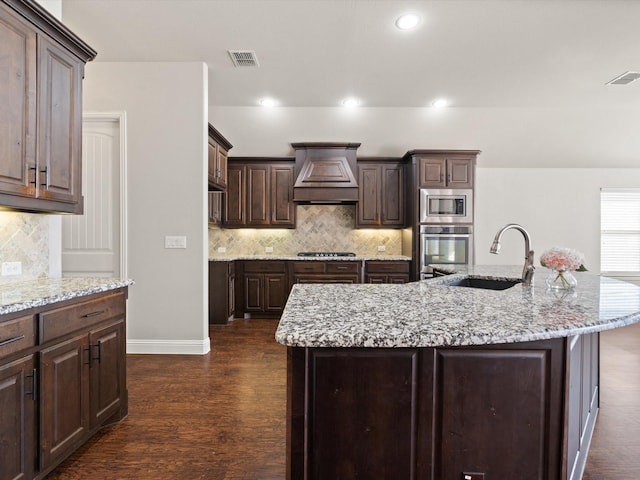 kitchen with custom exhaust hood, visible vents, appliances with stainless steel finishes, a sink, and dark brown cabinets