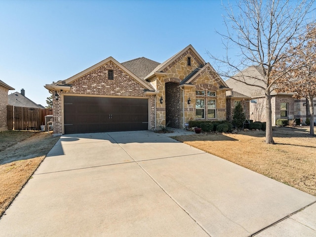 view of front of house with an attached garage, brick siding, fence, stone siding, and concrete driveway