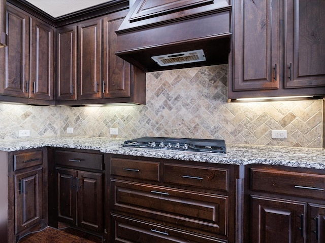 kitchen featuring premium range hood, stainless steel gas cooktop, light stone counters, and dark brown cabinetry