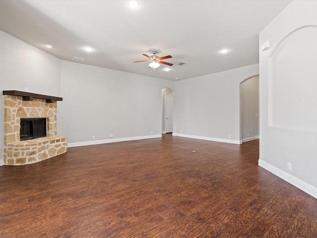 unfurnished living room featuring arched walkways, a fireplace, wood finished floors, visible vents, and a ceiling fan