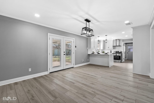 kitchen with white cabinetry, stainless steel range, kitchen peninsula, pendant lighting, and wall chimney range hood