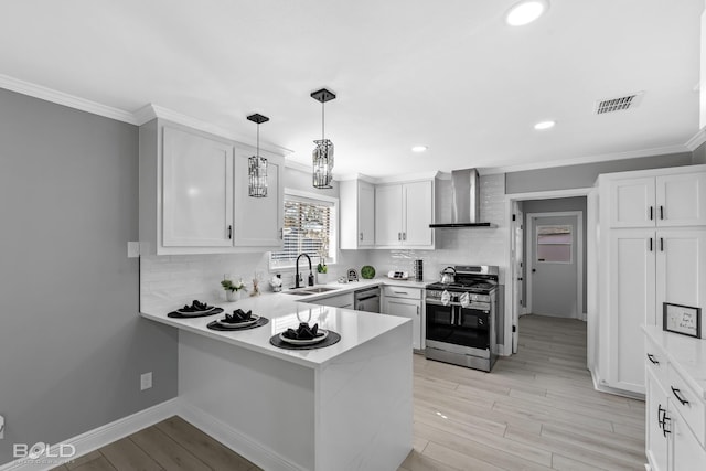 kitchen featuring appliances with stainless steel finishes, pendant lighting, white cabinetry, kitchen peninsula, and wall chimney range hood